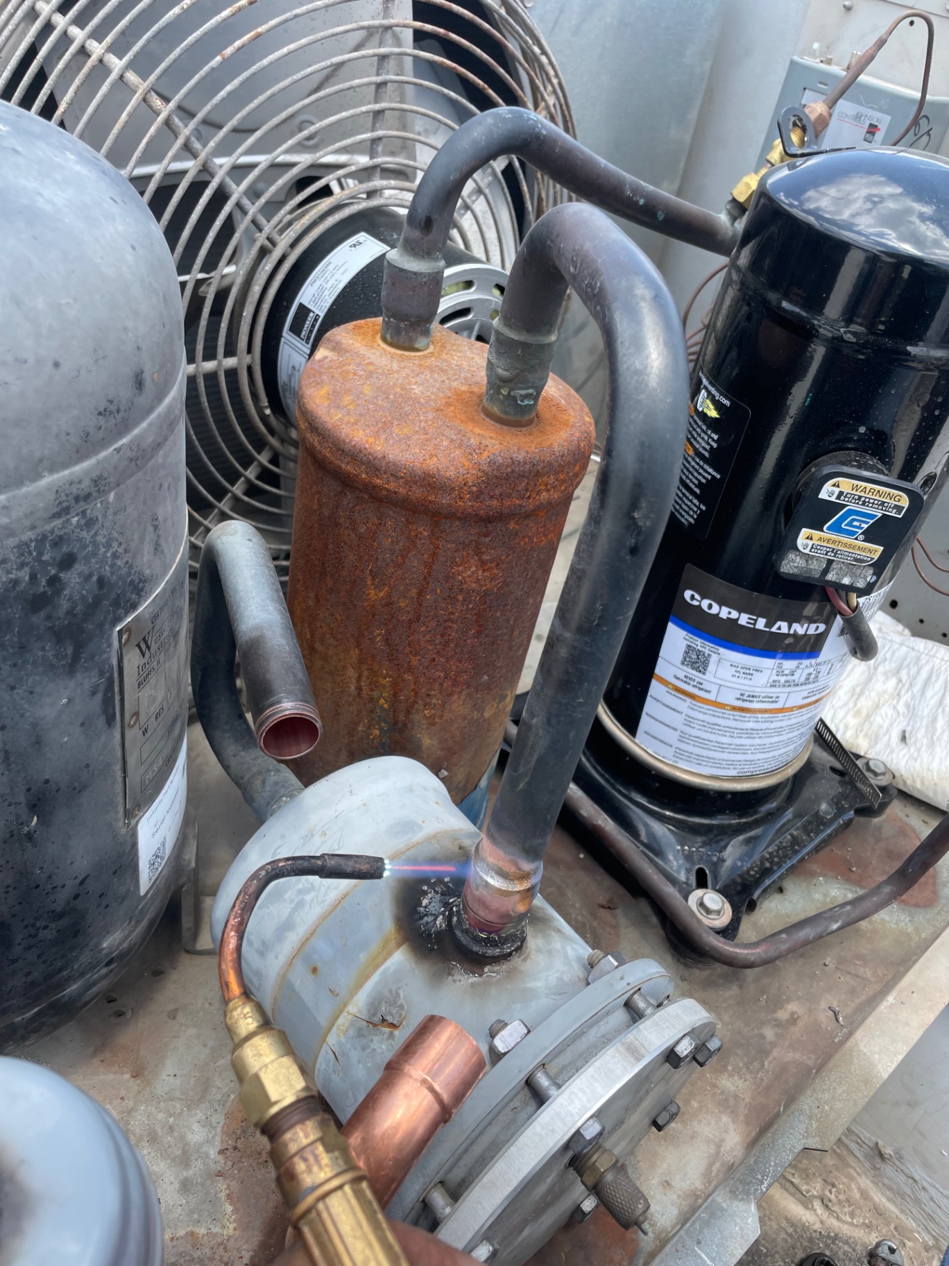 Technician brazing copper line set on a Copeland refrigeration compressor and receiver